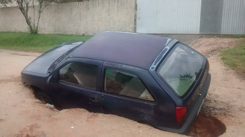 Chuva forma cratera e carro cai dentro